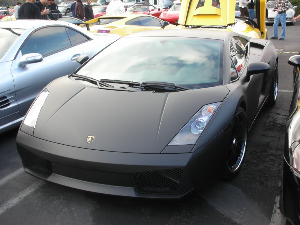 Matte black sports car parked next to a silver car and a yellow car with its hood up