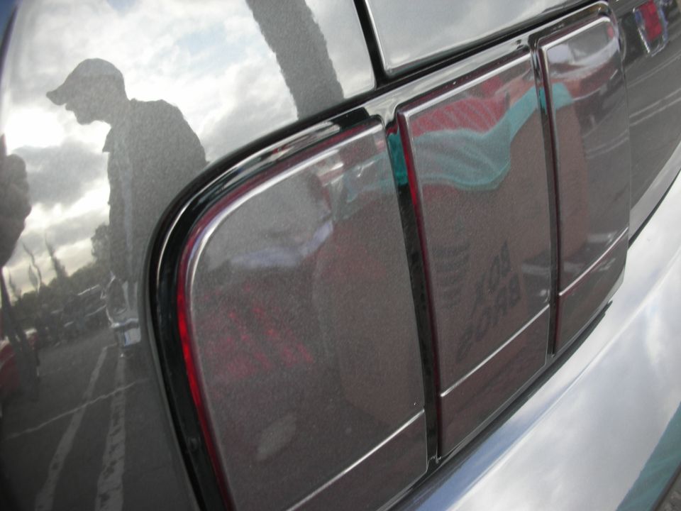 Gray car's rear quarter panel and taillight with reflection of a man wearing a cap