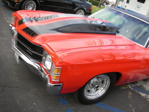 1998 Ford Crown Victoria - A bright red muscle car from the 1970s is parked next to other vehicles.