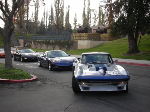1998 Ford Crown Victoria - A line of Corvettes drives down a street, led by a classic Stingray.