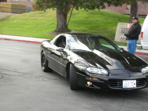 1998 Ford Crown Victoria - A black Chevrolet Camaro is shown from the front three-quarter view on a street with a grassy hill in the background.
