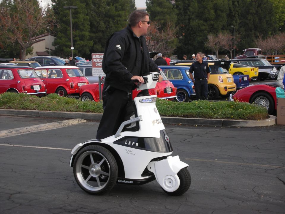 LAPD police segway with a man riding it, parked cars in background
