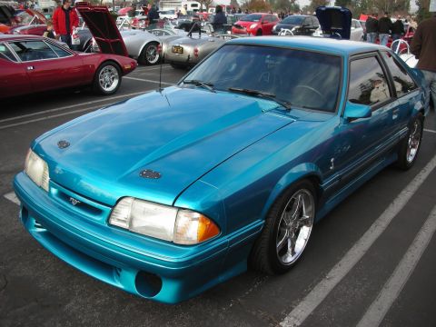 1998 Ford Crown Victoria - A teal coupe with an aftermarket hood scoop and chrome wheels is parked in a lot with other vehicles.