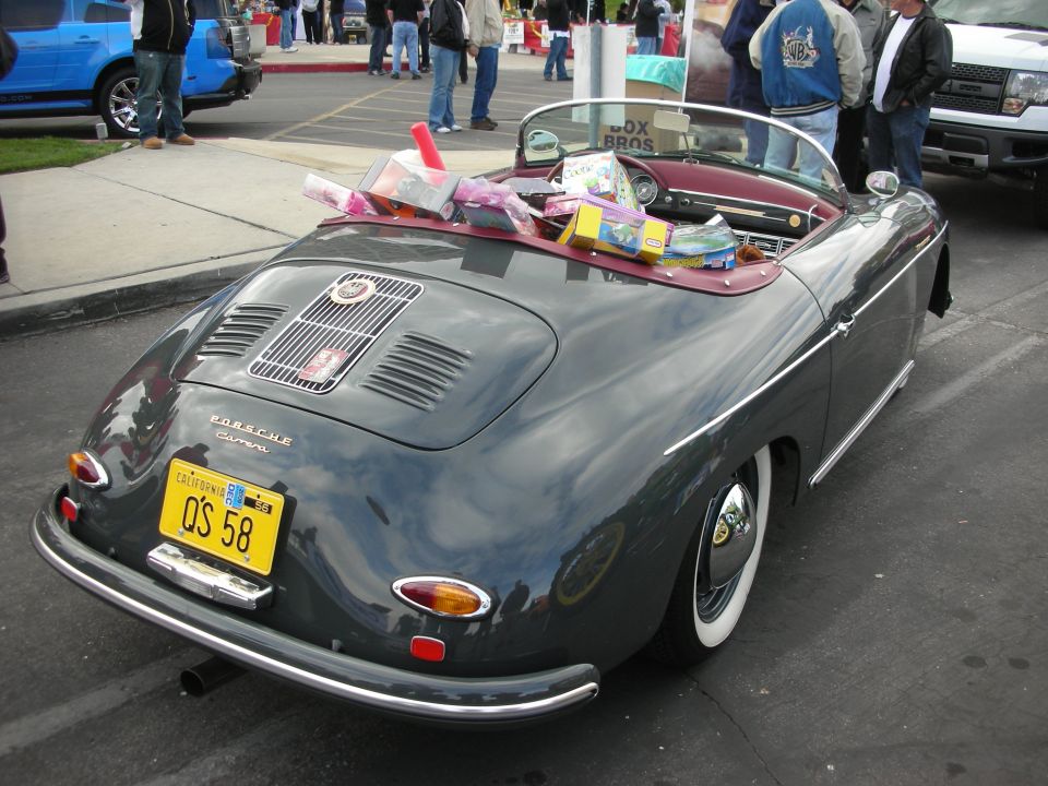 Dark gray convertible Porsche 356 Carrera with a yellow California license plate and items in the passenger seat