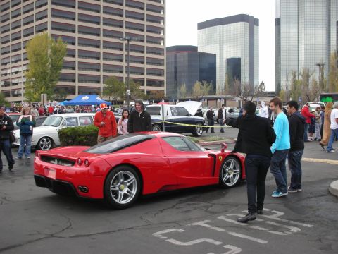 1998 Ford Crown Victoria - A bright red sports car is parked in a lot with people gathered around.