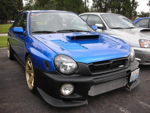 1998 Ford Crown Victoria - Modified blue Subaru Impreza WRX with aftermarket hood scoop and intercooler visible.
