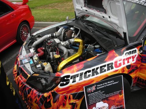 1998 Ford Crown Victoria - A modified Subaru WRX STI's engine bay is visible, adorned with flame graphics and custom parts.
