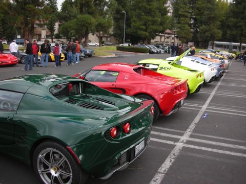1998 Ford Crown Victoria - A line of sports cars, including a green Lotus in the foreground, are parked in a lot.