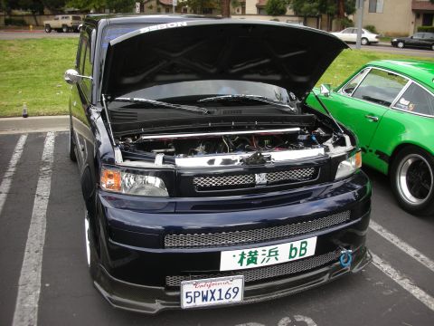 1998 Ford Crown Victoria - A dark blue Scion xB is parked next to a green Porsche, both with their hoods open.