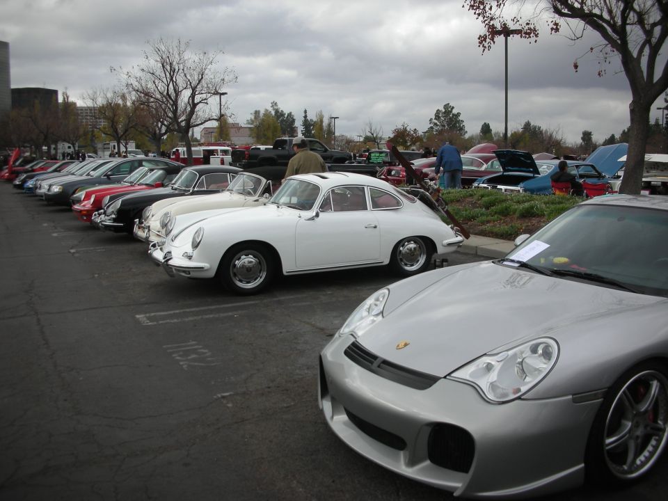 Silver Porsche 911 and white classic Porsche parked in a lot with other cars