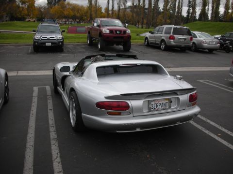 1998 Ford Crown Victoria - A silver convertible sports car is parked in a lot with other vehicles around it.