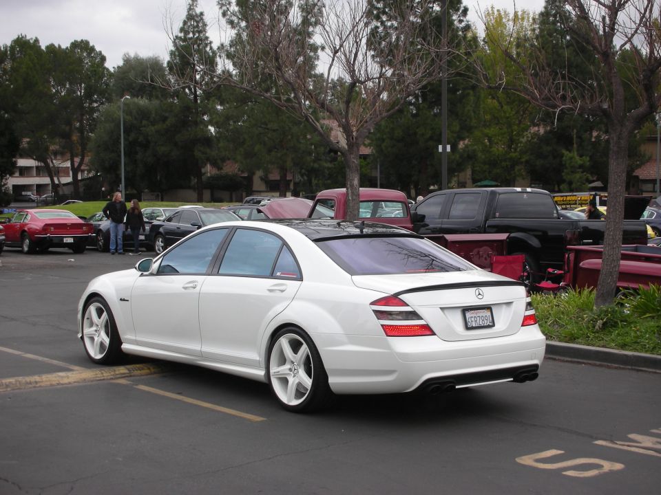White Mercedes-Benz sedan with tinted windows and white rims parked in a lot, rear view