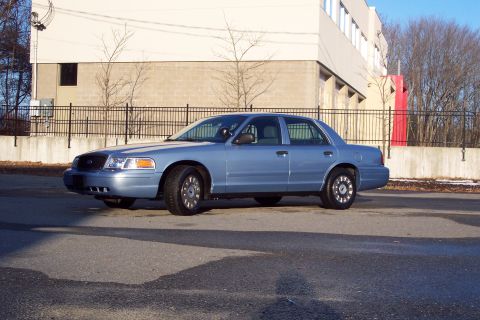 2001 Ford Crown Victoria - A silver sedan is seen from the side, parked on a street with a building in the background.