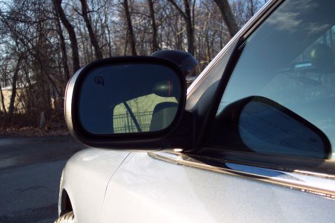 2001 Ford Crown Victoria - Close-up of a car's side mirror and chrome trim, with bare trees visible in the reflection and background.