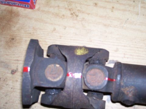 1991 Ford Bronco - Close-up of a rusty driveshaft U-joint and yoke assembly lying on a wooden bench, with red alignment paint marks striped across the flange,…