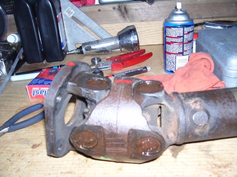 1991 Ford Bronco - A driveshaft component is shown on a workbench, surrounded by various tools and a can of spray lubricant.