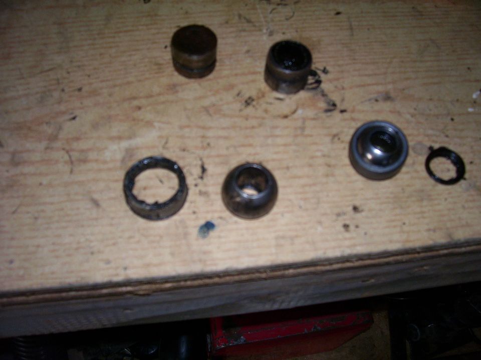 Several metal parts, possibly bearings or bushings, laid out on a wooden surface