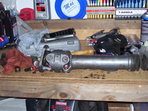 1991 Ford Bronco - A driveshaft rests on a wooden workbench alongside various tools and automotive fluids.