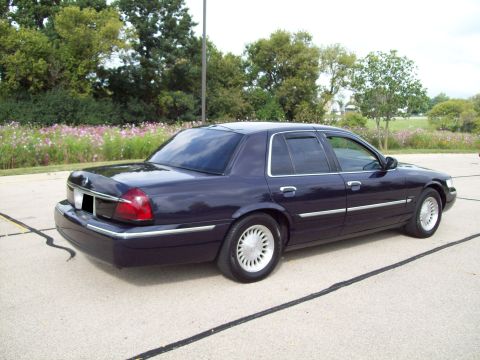 1999 Mercury Grand Marquis - A dark navy blue Mercury Grand Marquis full-size sedan photographed from the rear three-quarter angle, showing the passenger side, chrome t…