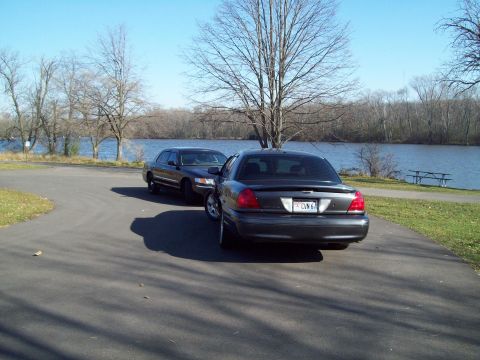 1999 Mercury Grand Marquis - Two Mercury Grand Marquis sedans are parked near a body of water on a clear day.