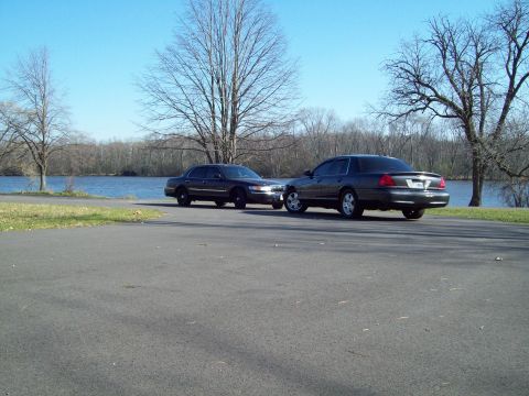 1999 Mercury Grand Marquis - Two Ford Crown Victoria police interceptors are parked near a body of water on a clear day.