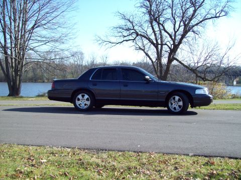1999 Mercury Grand Marquis - Side view of a 1999 Mercury Grand Marquis parked outdoors with trees and water in the background.