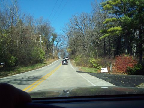 1999 Mercury Grand Marquis - Two cars drive down a tree-lined road on a clear day.