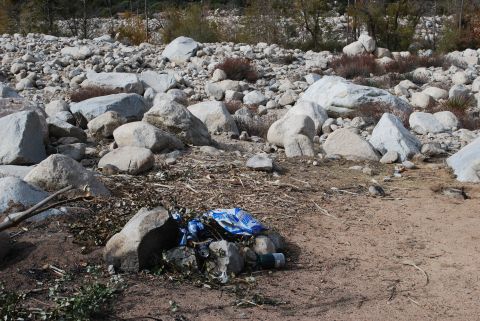 1996 Ford Bronco - Debris from a campsite is scattered among rocks and dry brush in an outdoor setting.