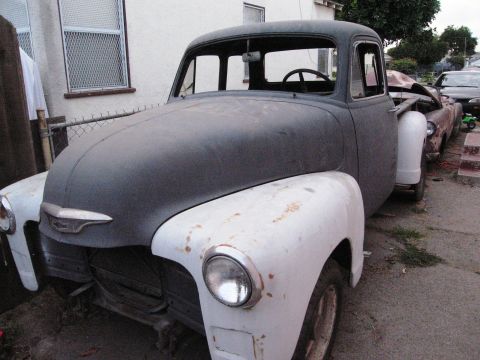 1986 Ford Bronco - A vintage pickup truck, likely from the mid-1950s, sits parked on a street next to another vehicle.