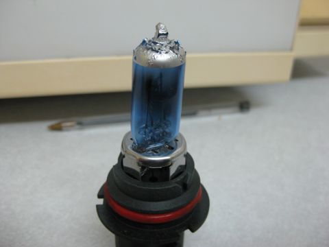 1994 Ford Thunderbird - A close-up view of a damaged automotive headlight bulb with a blue glass enclosure.