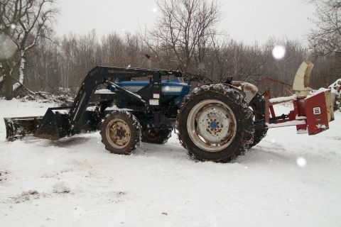 2000 Chevrolet Tahoe - A blue tractor equipped with a front loader and a snow blower sits in a snowy field.