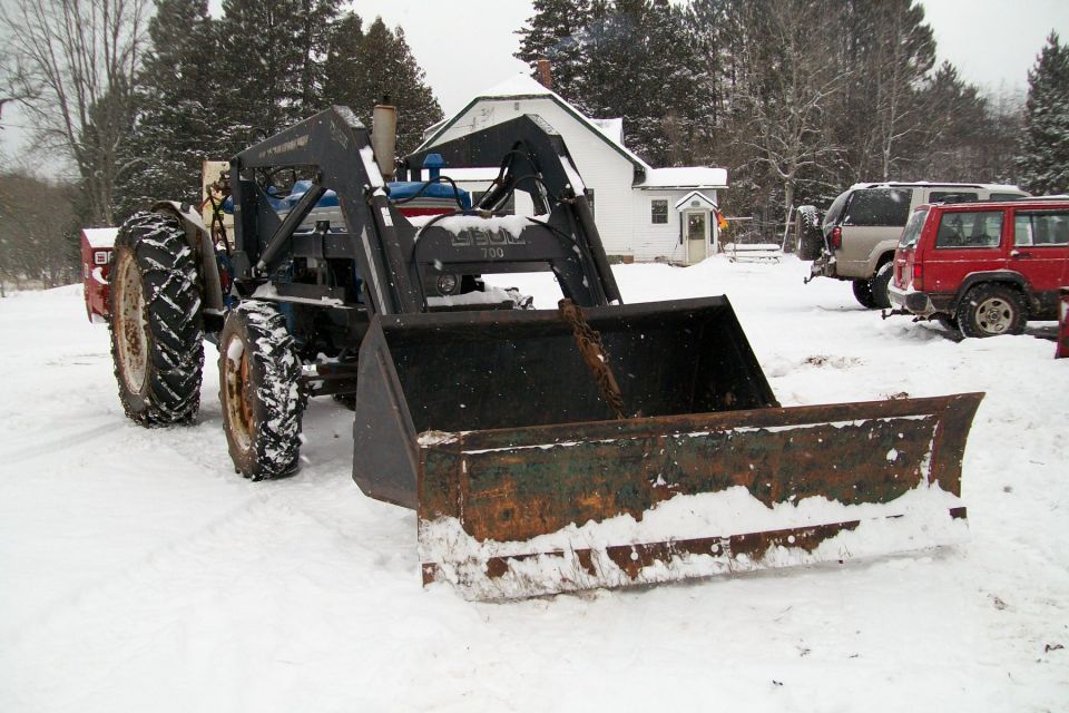 Tractor with front loader covered in snow, two SUVs in background