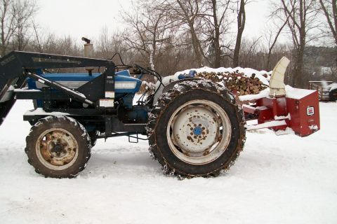 2000 Chevrolet Tahoe - A blue tractor equipped with a loader and a red snow blower attachment sits in a snowy outdoor environment.