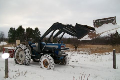 2000 Chevrolet Tahoe - A blue tractor equipped with a front loader is seen in a snowy field, ready for work.
