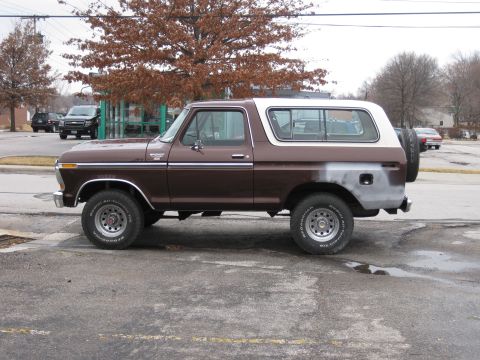1978 Ford Bronco - A brown and white 1978 Ford Bronco is parked on a wet asphalt surface with a tree in the background.