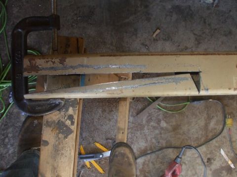 1995 Ford Bronco - A metal component is being cut while secured by a clamp, with various tools and a workshop floor in the background.