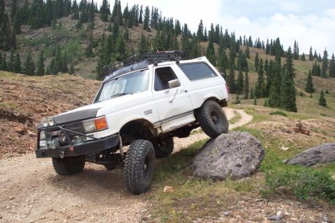 1990 Ford Bronco - This white 1990 Ford Bronco navigates a challenging rocky terrain on a mountain trail, its off-road capabilities.