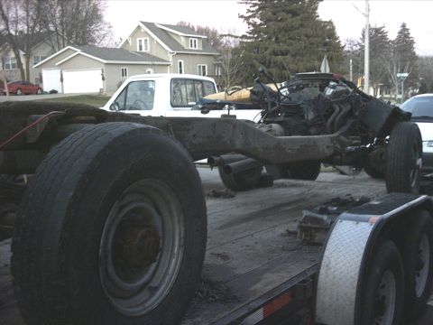 1954 Ford F-100 - A disassembled truck chassis with its engine is being transported on a trailer.