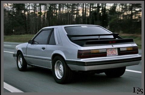 1986 Ford Mustang - Silver 1986 Ford Mustang coupe seen from the rear on a highway.