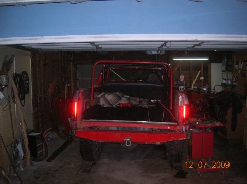 1985 Ford Bronco - The rear of a red Ford Bronco is visible in a garage, showing its open tailgate and roll cage.
