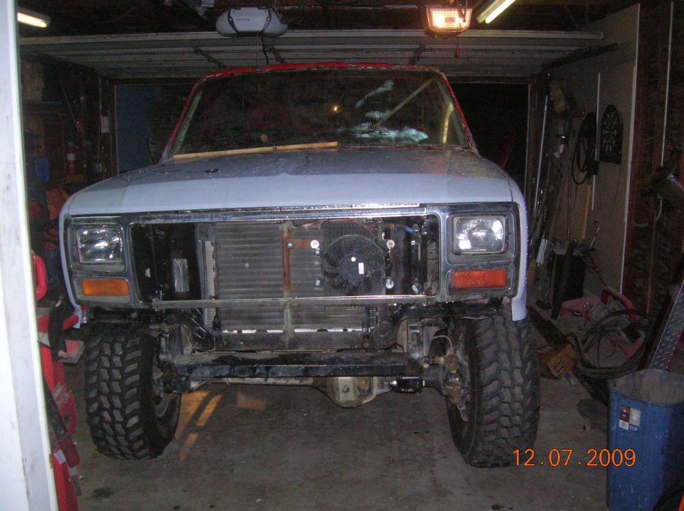 Front view of a Ford Bronco in a garage, undergoing repairs. The grille is removed, showing the radiator and fan