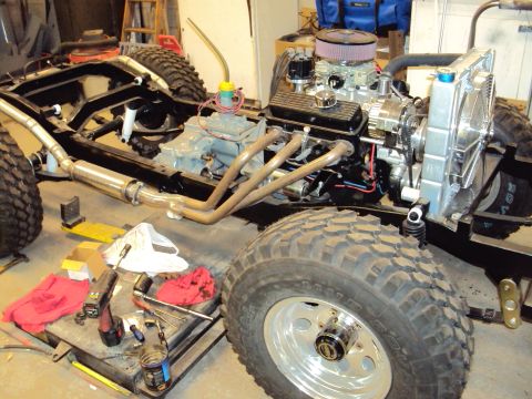 1948 Jeep Wrangler - A Jeep CJ frame is shown with its engine, radiator, and exhaust headers installed, alongside large off-road tires.