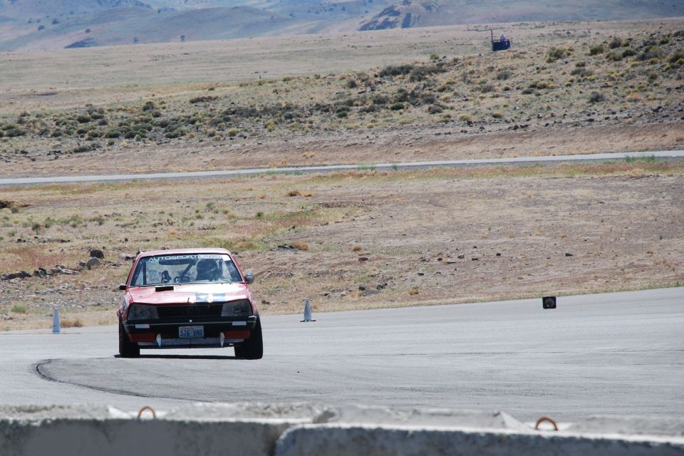 Red track-prepped sedan cornering head-on at a desert racetrack