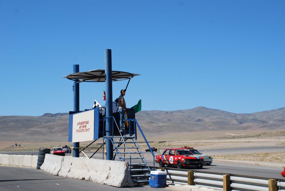 Red number 21 race hatchback on desert track passing a flag marshal station.