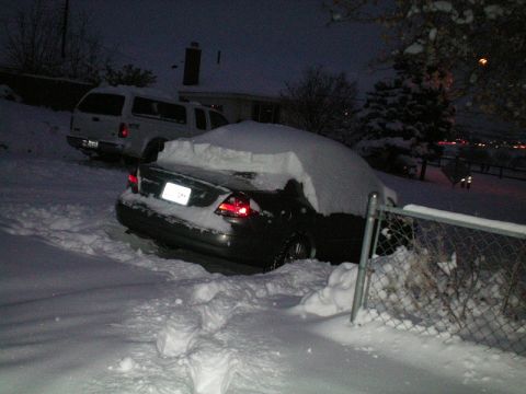 2003 Ford Taurus - A dark sedan and a white pickup truck are covered in snow during a winter storm.
