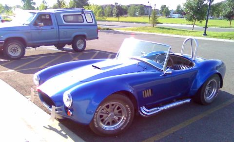 2006 Ford E350 - A classic blue convertible sports car is parked in a lot next to a blue pickup truck with a camper shell.