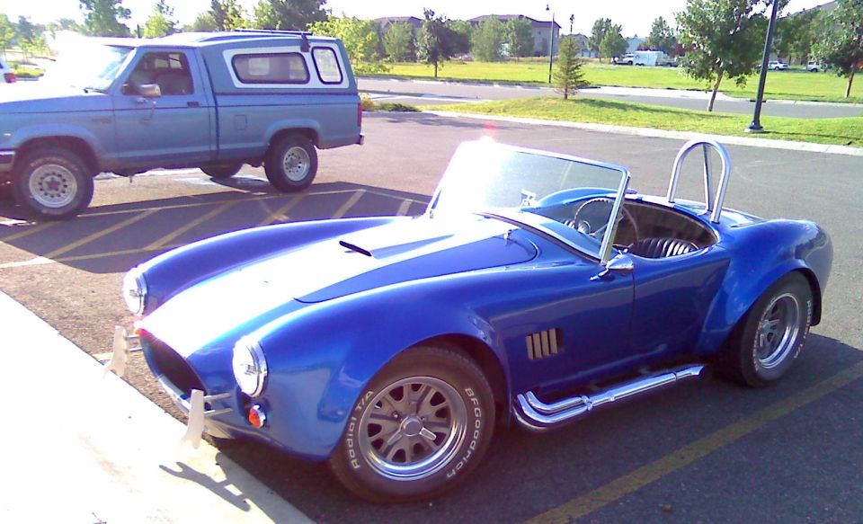 Blue convertible sports car with side pipes and roll bar, parked next to a blue pickup truck