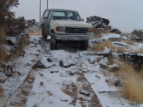 1989 Ford Bronco - Two-tone Ford Bronco navigates a snowy, rocky off-road path.