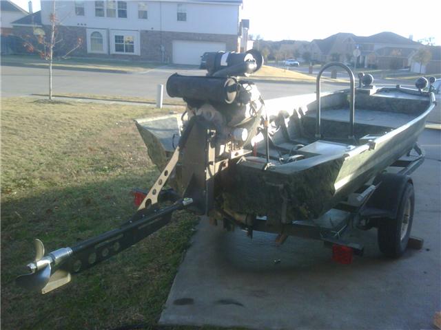 Green boat with outboard motor on a trailer parked on a driveway
