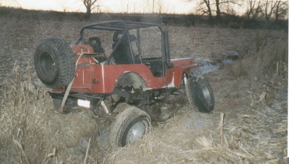 Red Jeep CJ with roll bar and spare tire sitting in a muddy field